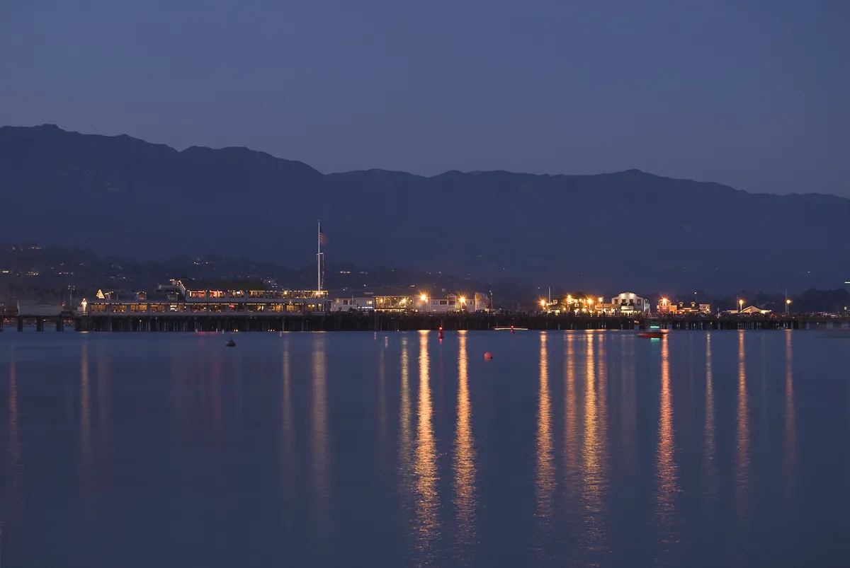 Stearns Wharf and the Santa Barbara waterfront lit up at dusk below the mountains